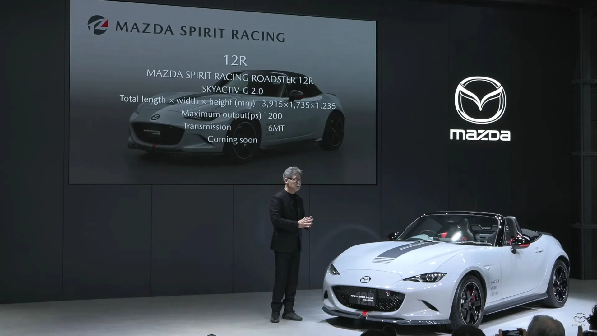 A photo from the press conference showing the MX-5 12R on a stage in front of a speaker and a slide about the car