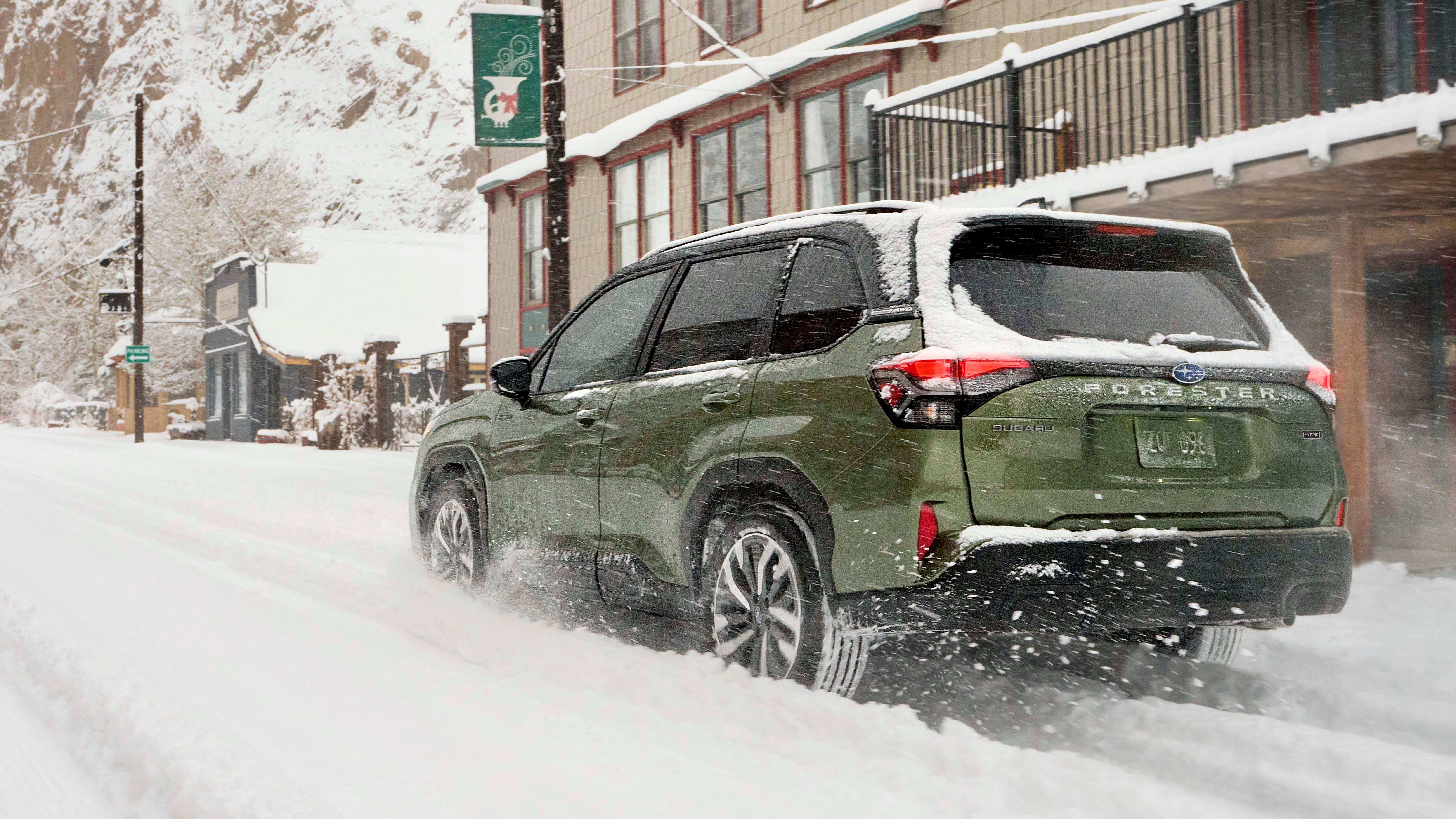 a rear shot of the green Forester Hybrid in the snow in front of a building