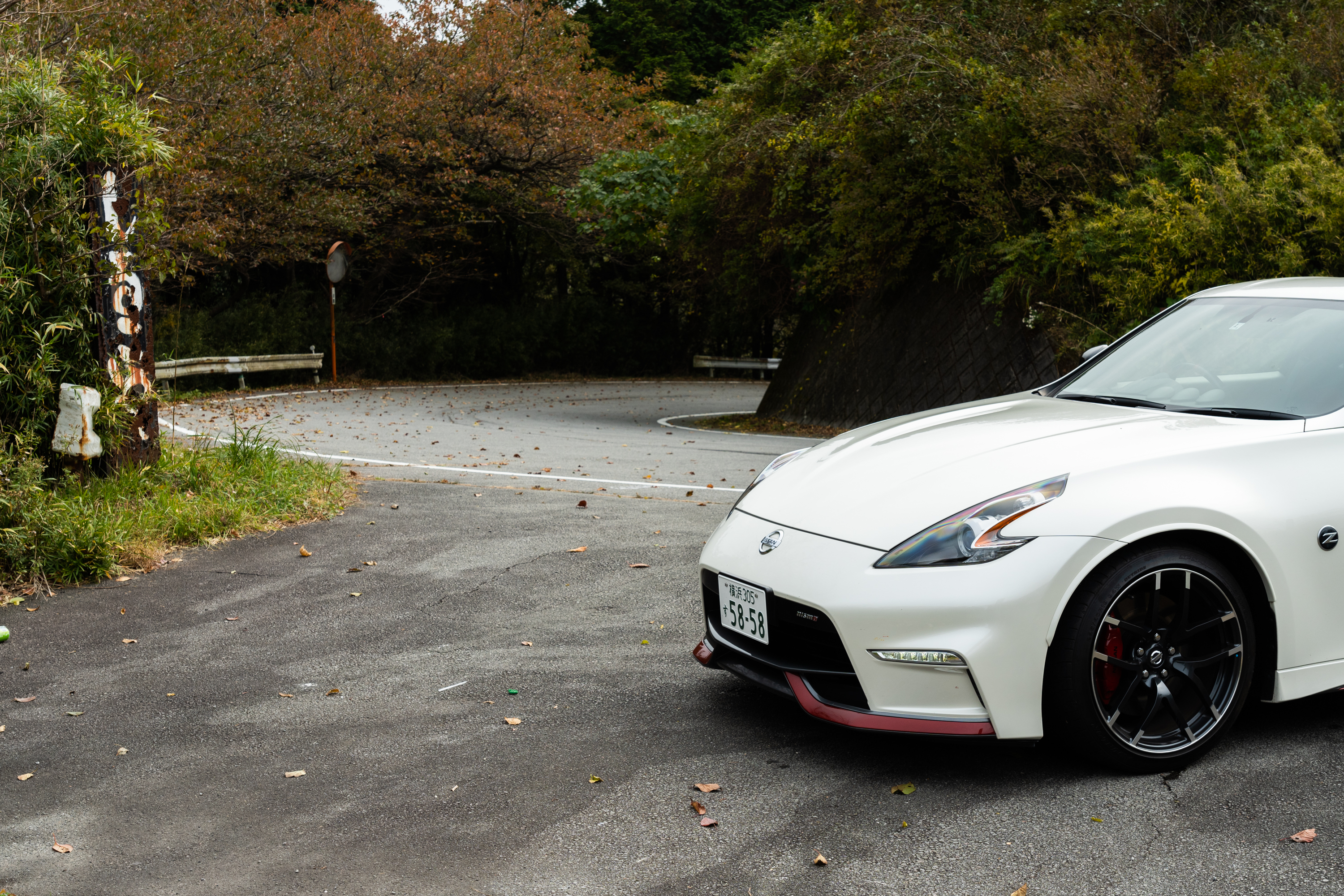 a white nissan fairlady z nismo parked at the edge of a mountain road in japan in the autumn