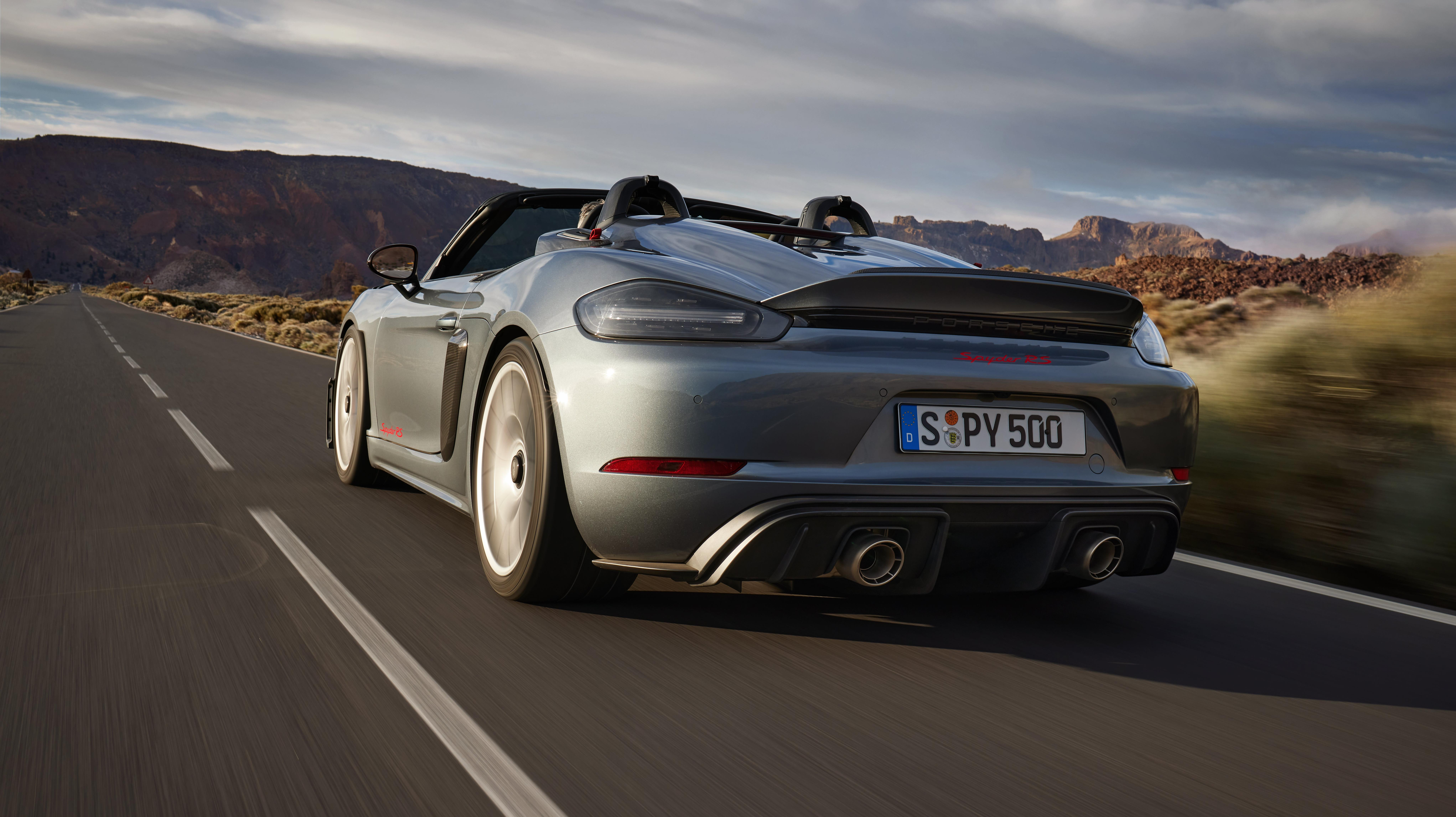 A rear 3/4 shot of a gray Porsche 718 Spyder RS driving through the desert