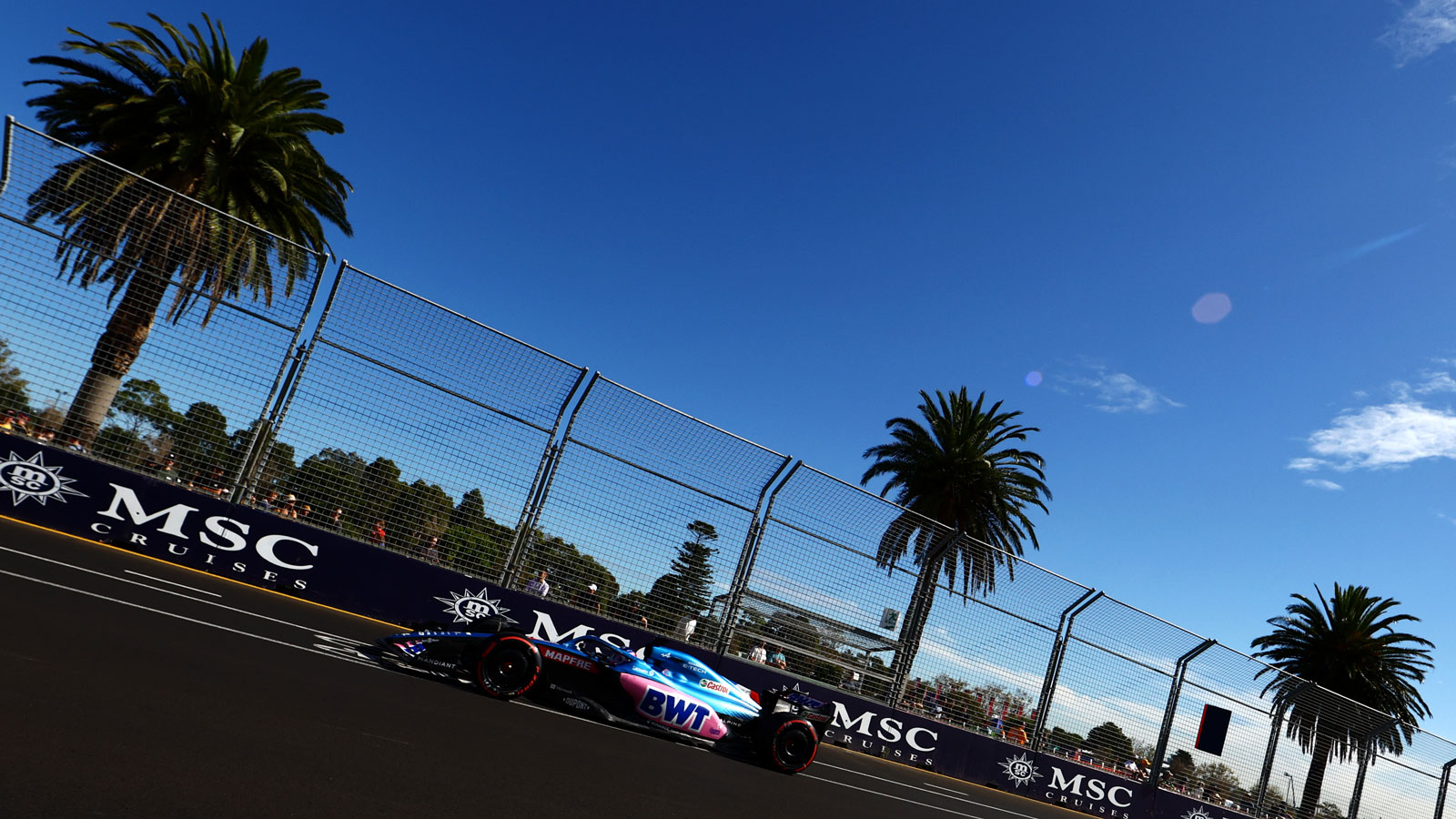 A photo of Fernando Alonso driving past a line of palm trees. 