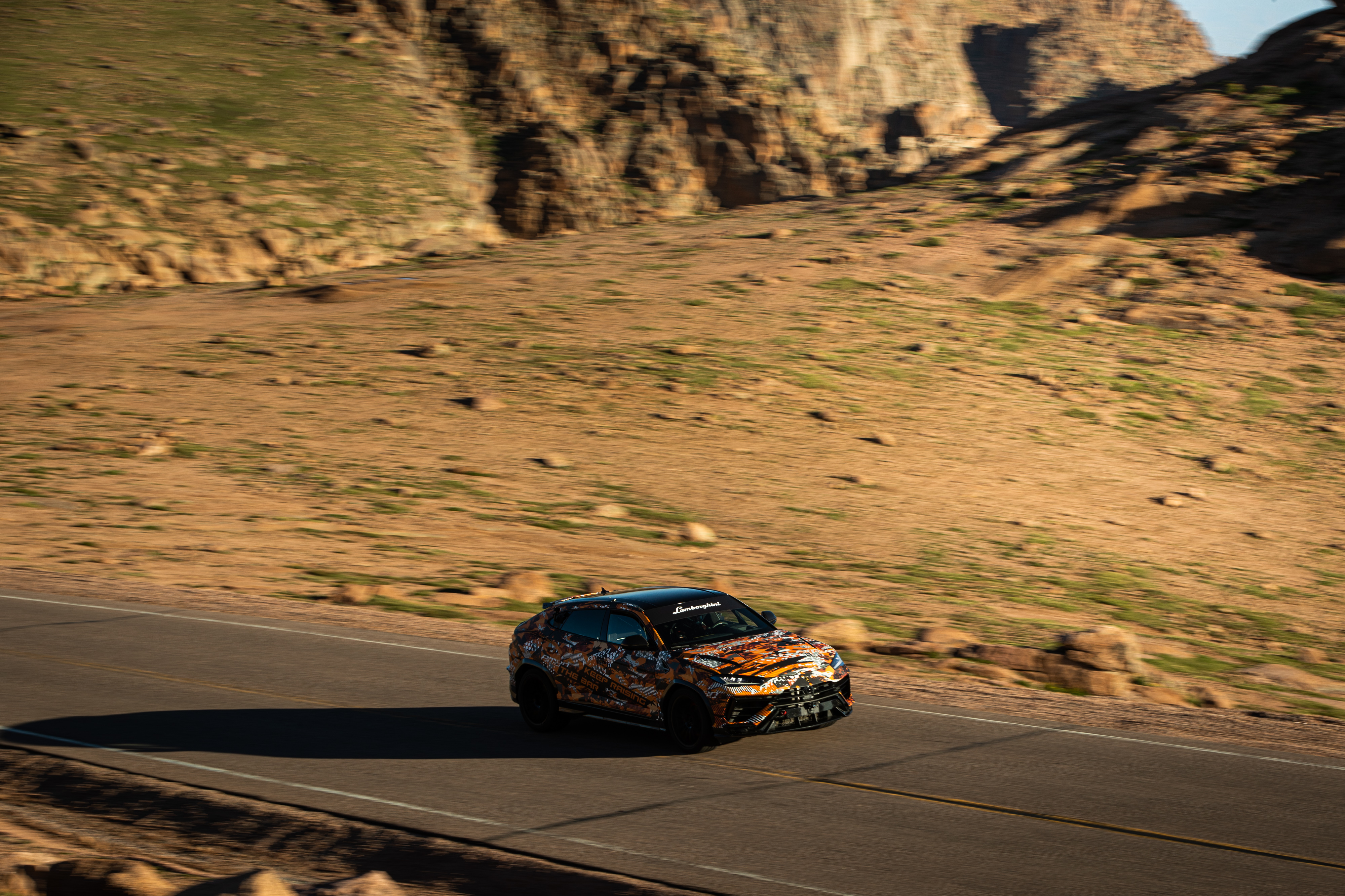 Lamborghini Urus SUV at speed on a mountain road.