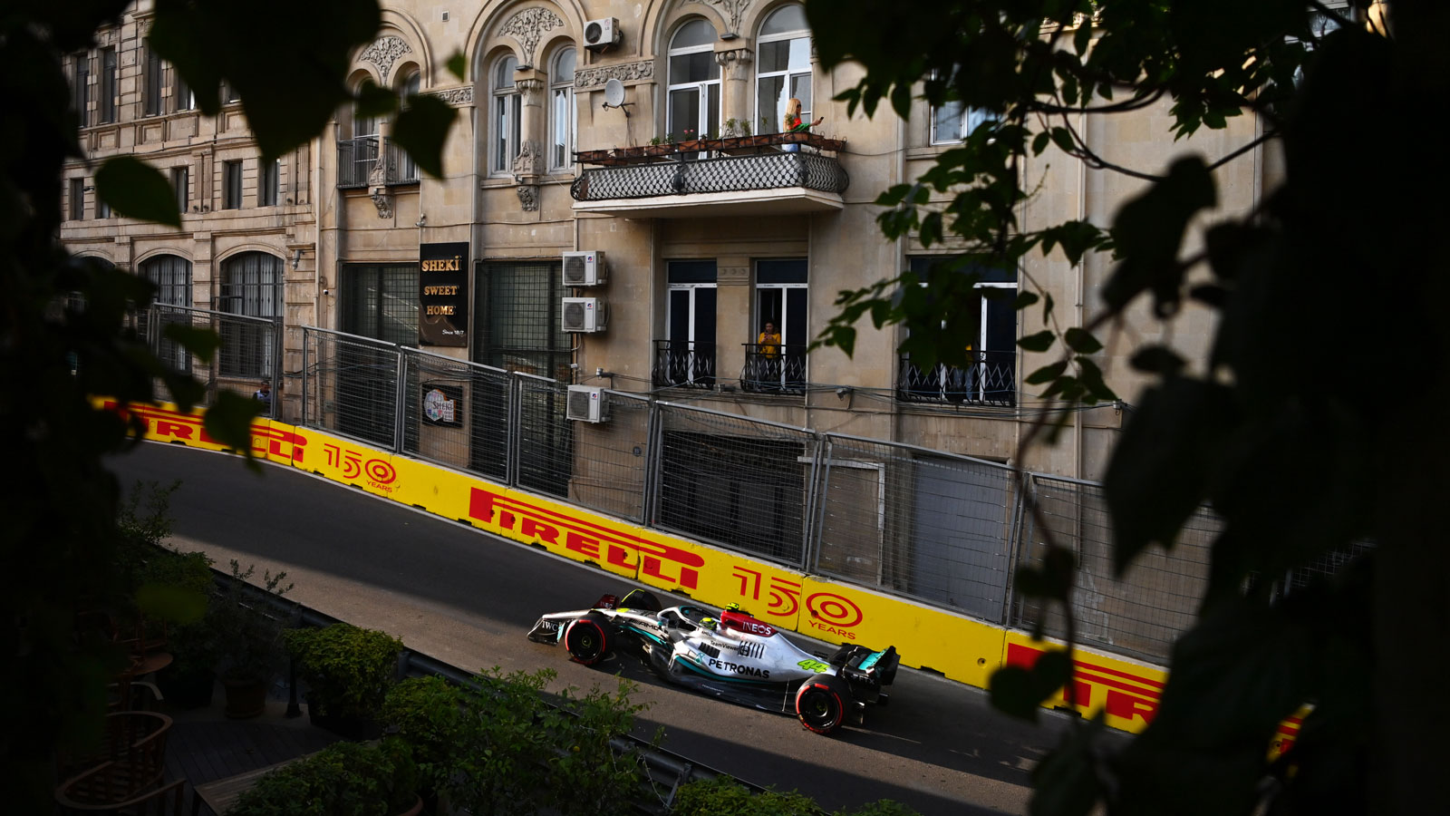 Lewis Hamilton drives his silver W13 race car past an old apartment block in Baku. 