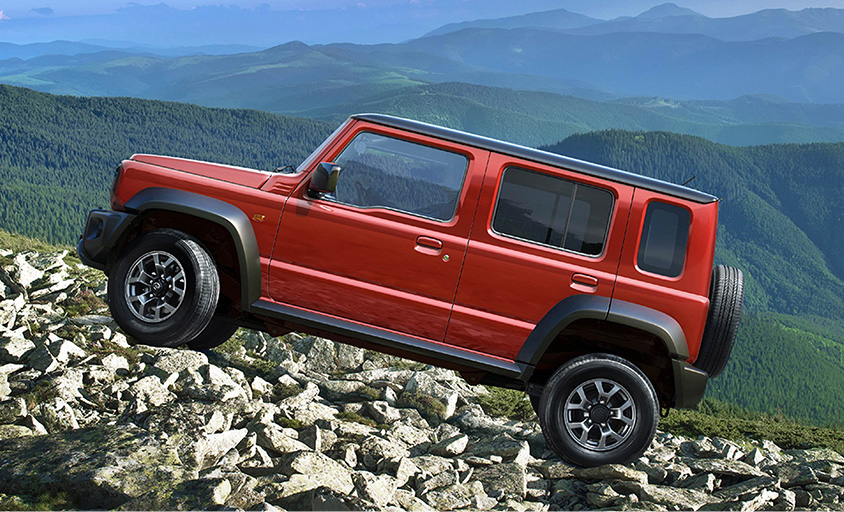 a red jimny nomade driving up a rocky slope in front of a view of mountains