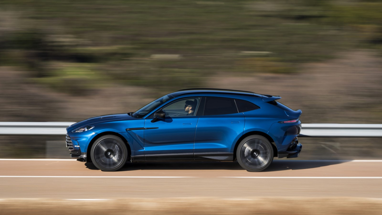 A photo of an Aston Martin DBX SUV driving on a highway. 