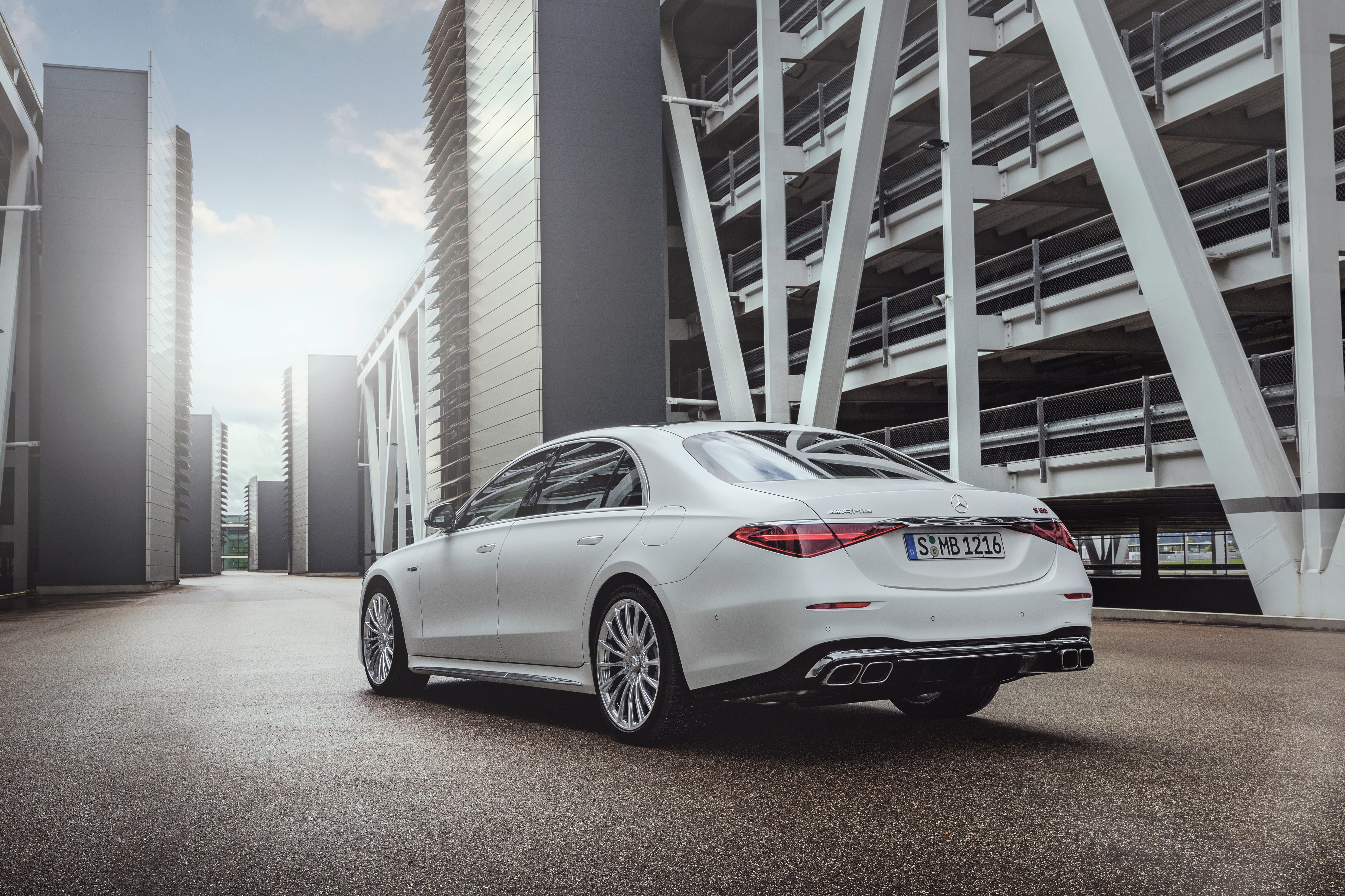 a white 2023 mercedes-amg s 63 e performance sedan seen from the rear, parked in a generic industrial complex surrounded by parking garages